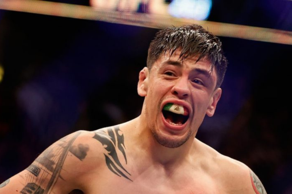 MMA-vechter met een groen bitje in de mond schreeuwt tijdens een UFC-gevecht, zichtbaar vol emotie en adrenaline.