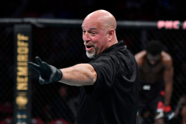 Scheidsrechter in MMA-octagon geeft signaal tijdens gevecht, met vechter op de achtergrond.