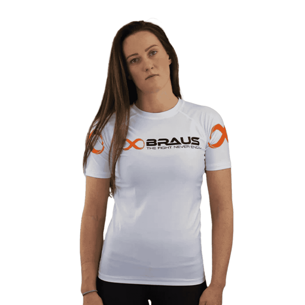 Een afbeelding van de voorkant van een witte damesrashguard met korte mouwen van Braus. Het shirt heeft oranje logo's en de tekst "Braus - The Fight Never Ends". Een vrouw kijkt recht naar de camera.