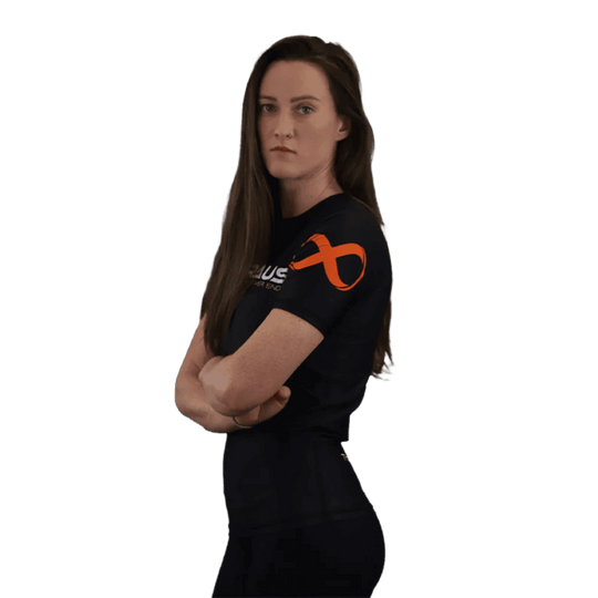 Een afbeelding van de zijkant van een zwart damesrashguard met korte mouwen van Braus. Het shirt heeft een oranje logo op de mouw en een zelfverzekerde vrouw met haar armen gekruist.