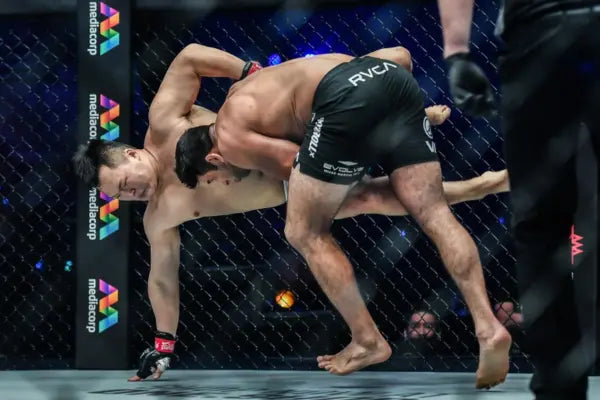 Een MMA-vechter voert een explosieve double leg takedown uit, terwijl de tegenstander uit balans raakt en naar de grond wordt gedwongen.