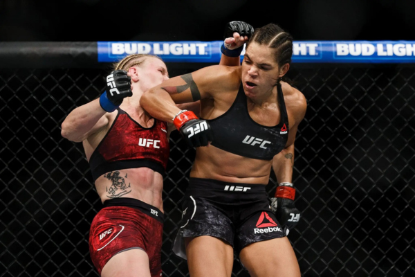 Twee vrouwelijke MMA-vechters in actie tijdens een UFC-gevecht, met één vechter die een stoot ontvangt.