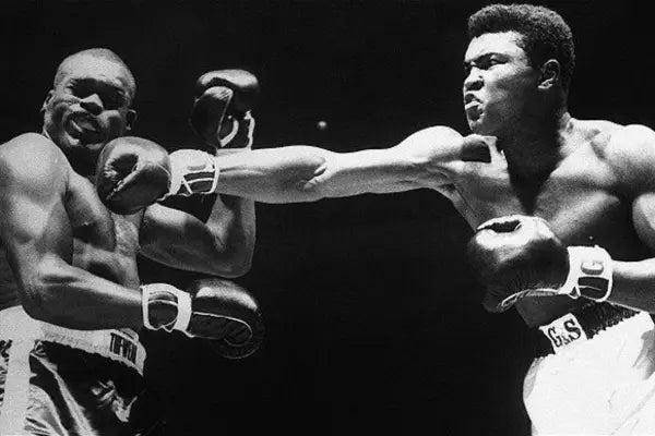 Zwart-wit foto van twee boksers in actie waarbij een vechter een lange, krachtige rechterstoot uitdeelt terwijl de tegenstander naar achteren wijkt.