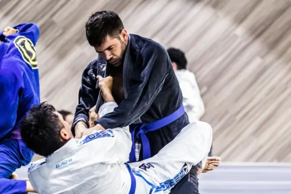 Twee BJJ-vechters in gi tijdens een intens gevecht op de mat, waarbij de staande vechter dominante grips probeert te leggen om controle te nemen.