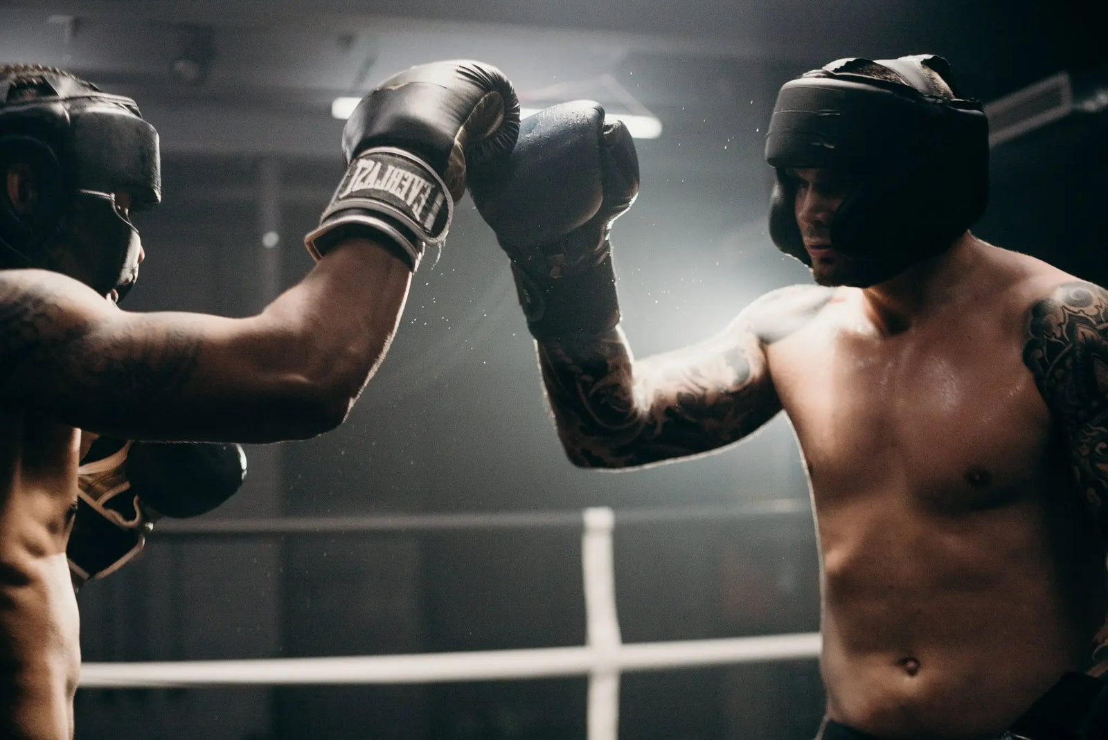 Twee boksers met hoofdbescherming geven elkaar een sportieve boks in de ring.