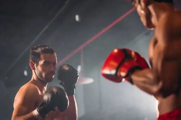 Twee boksers staan klaar om te sparren in een verlichte trainingsruimte.