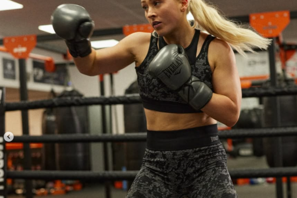Vrouw in sportoutfit traint met zwarte Everlast bokshandschoenen in een boksschool.