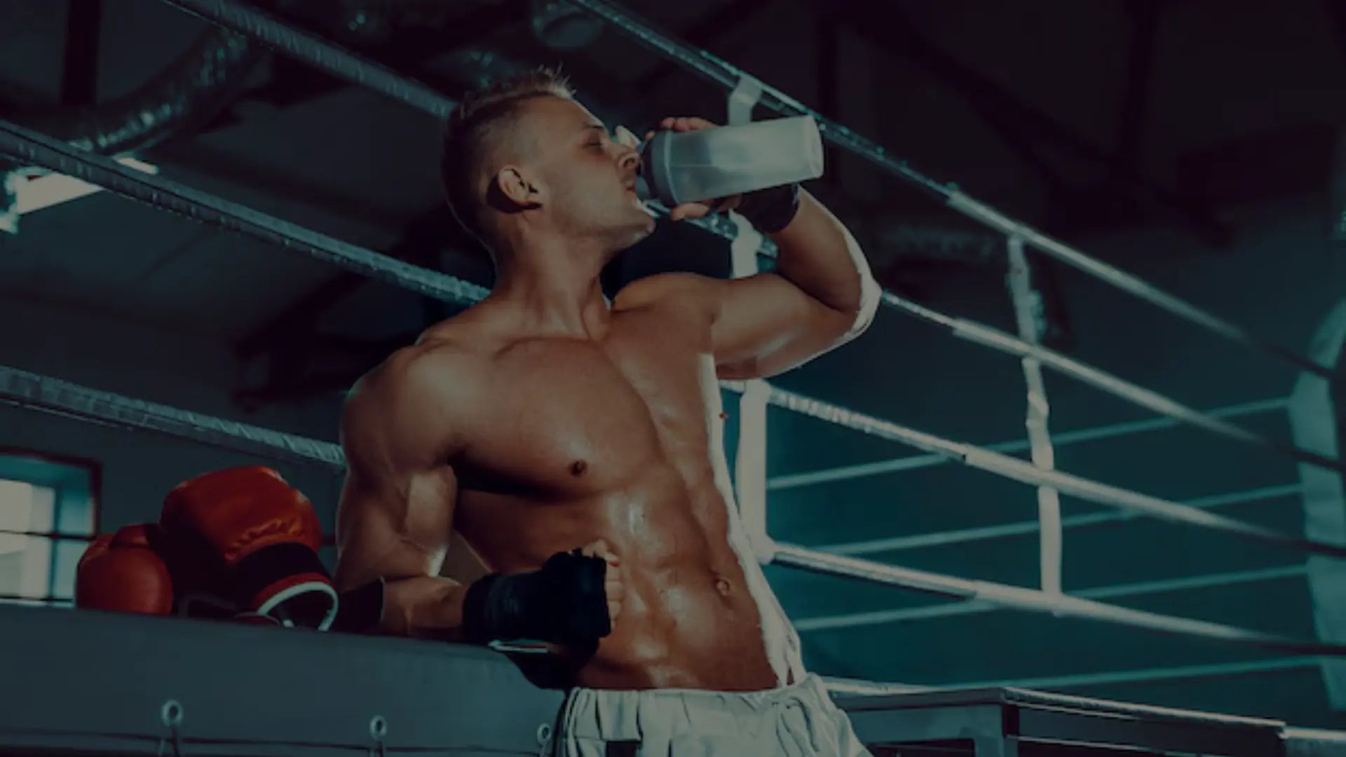 Een sporter met bokshandschoenen naast zich drinkt uit een bidon terwijl hij uitrust aan de rand van de boksring na een intensieve training.