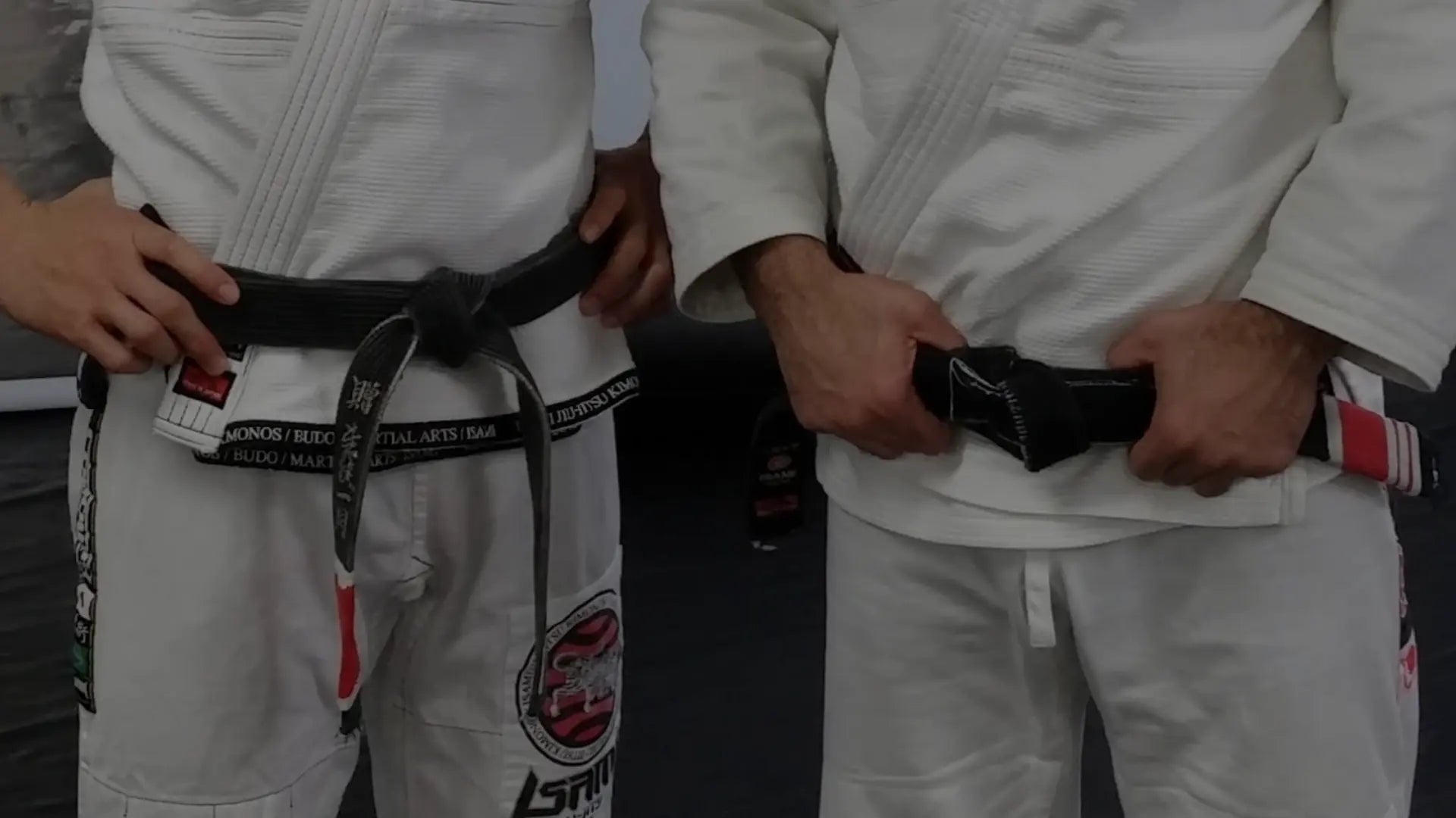 Twee BJJ-beoefenaars in witte gi’s die hun zwarte banden vastmaken, gefocust op voorbereiding voor training of competitie.
