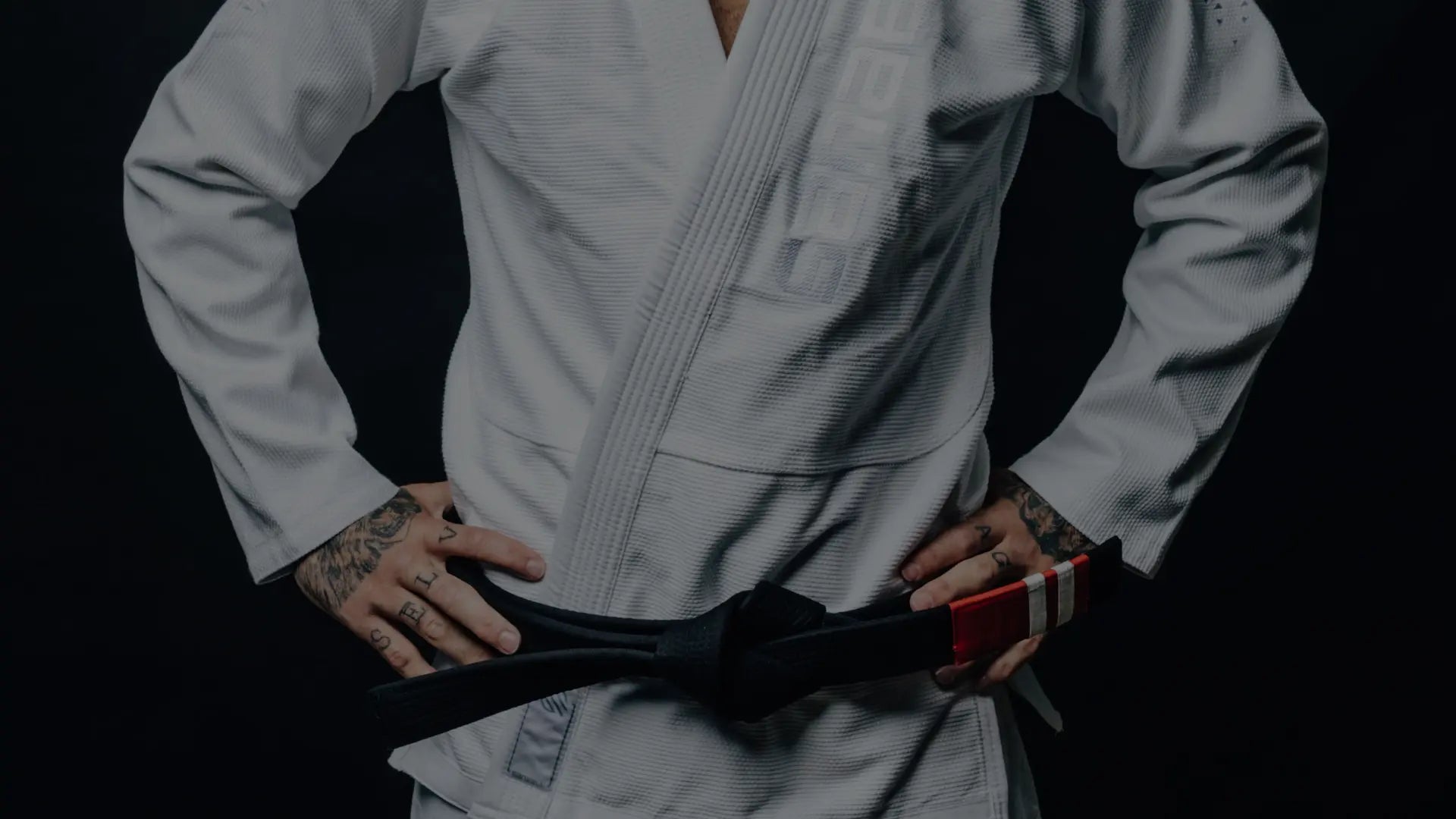 Close-up van een BJJ-beoefenaar in een witte gi met een strakgeknoopte zwarte band, handen op de heupen voor training of competitie.