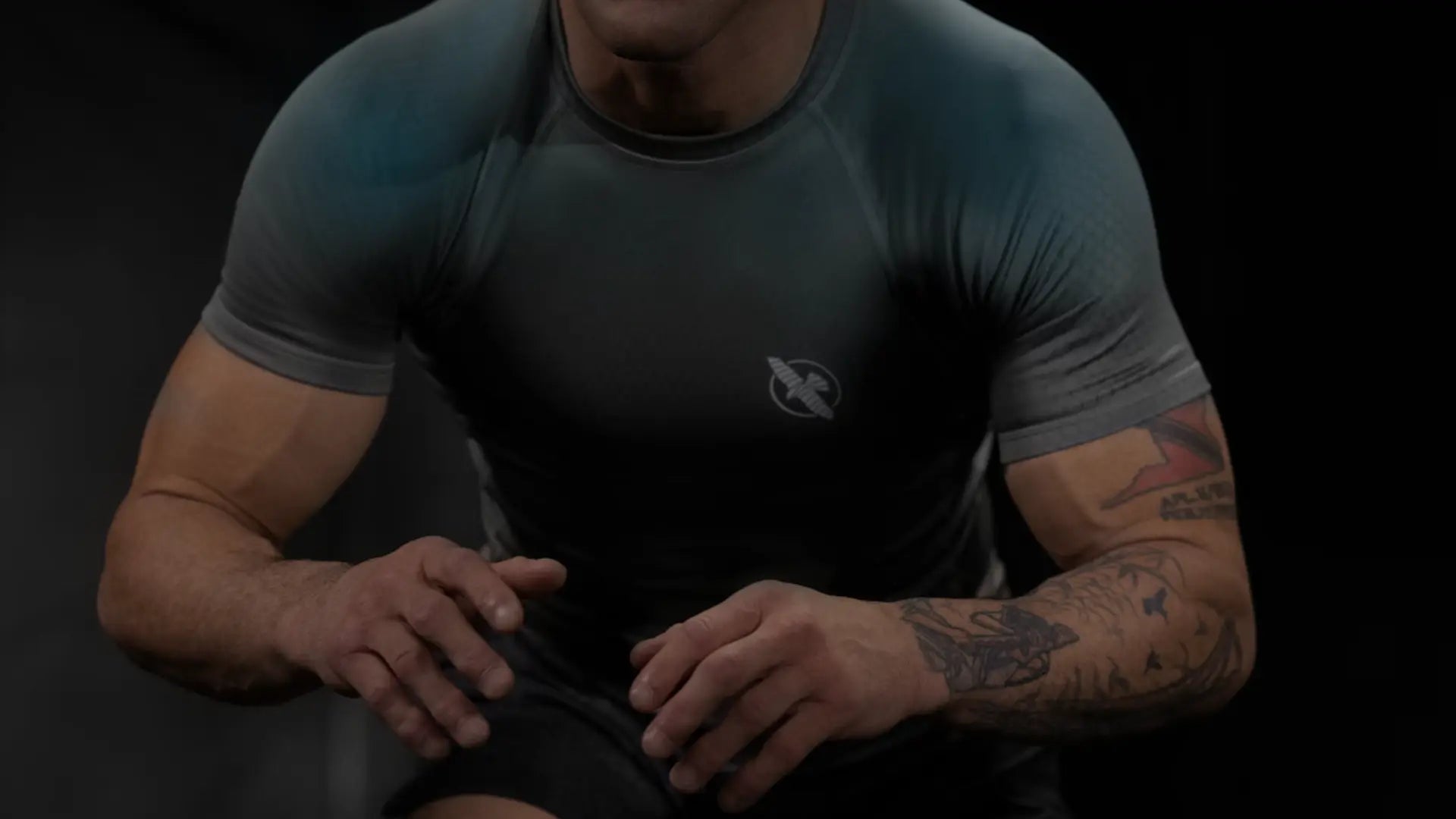 Close-up van een BJJ-beoefenaar die traint in een zwarte rashguard van Hayabusa, met een gefocuste houding en zichtbare arm­tatoeages.