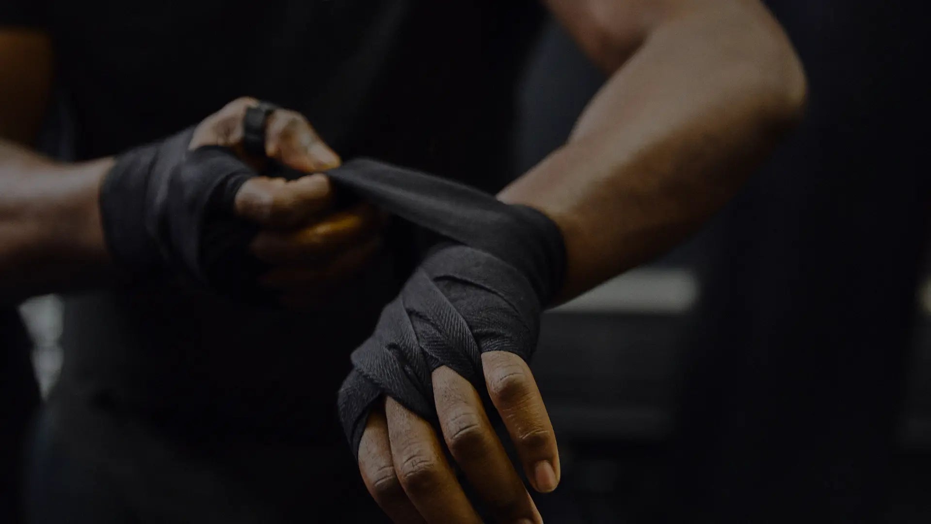 Close-up van een sporter die zwarte handwraps strak om zijn handen wikkelt ter voorbereiding op een intensieve bokstraining.