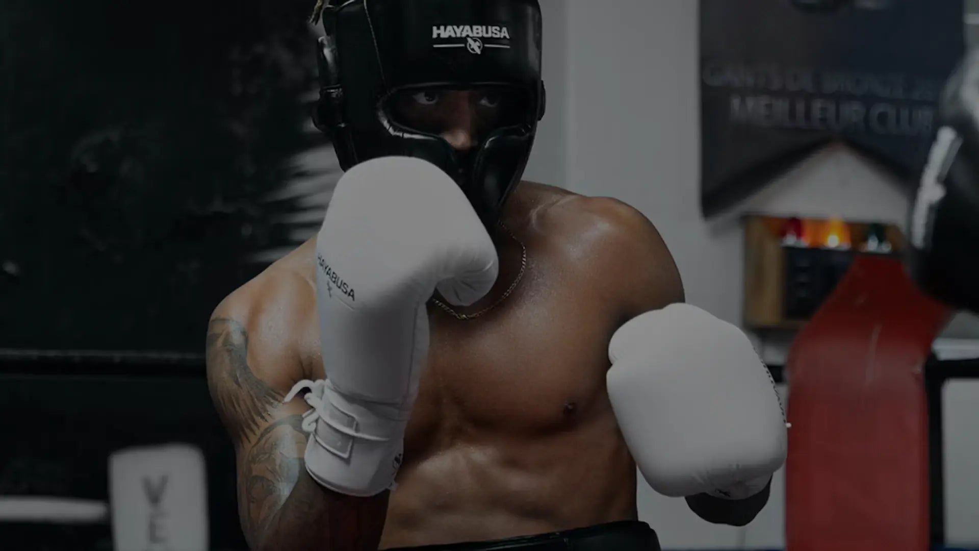 Een bokser in de ring met witte Hayabusa-handschoenen en een zwarte hoofdbeschermer, klaar om stoten te verdedigen en uit te delen.