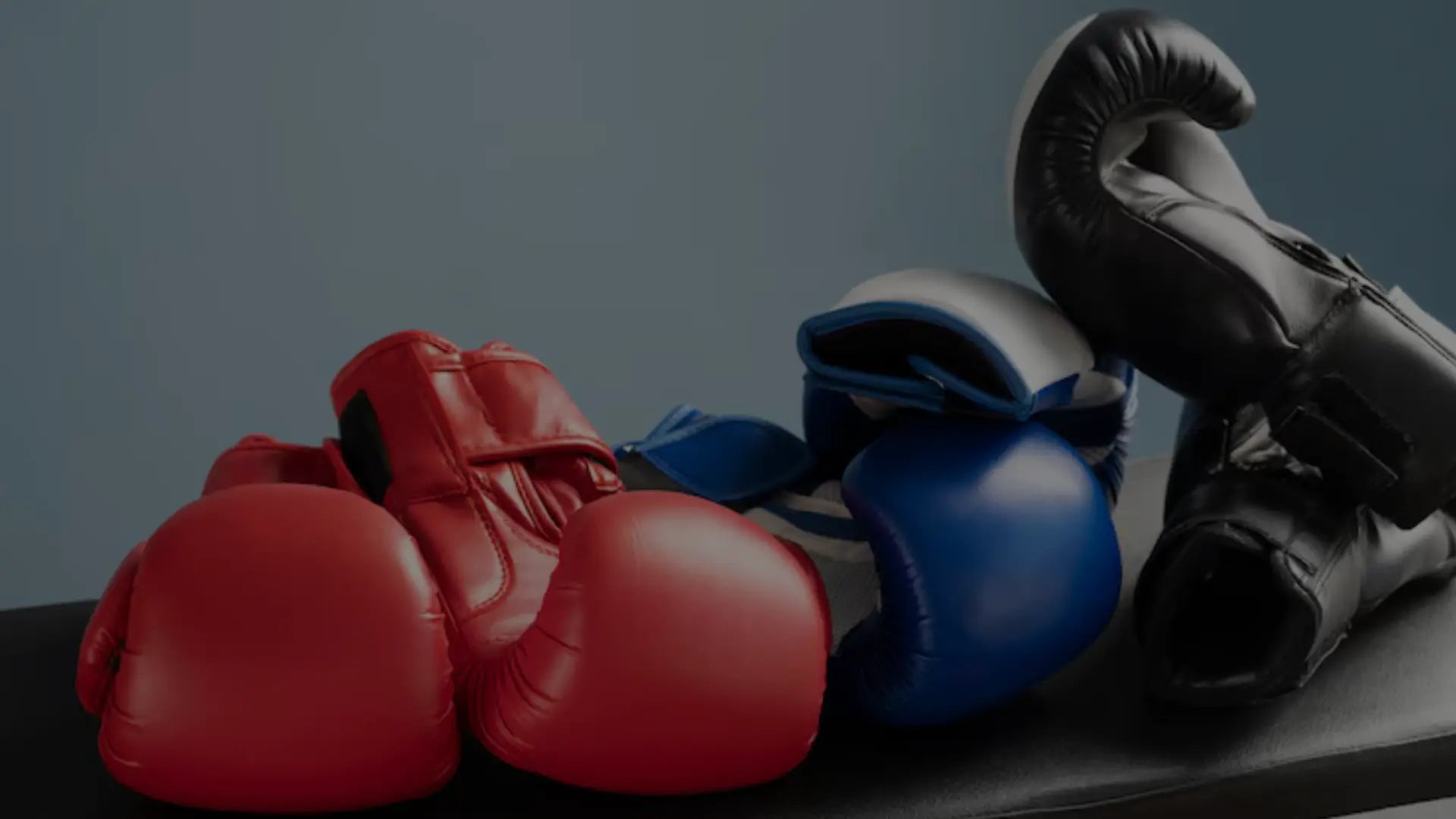 Verschillende bokshandschoenen in rood, blauw en zwart liggen samen op een bank, geschikt voor bokstraining en sparren.