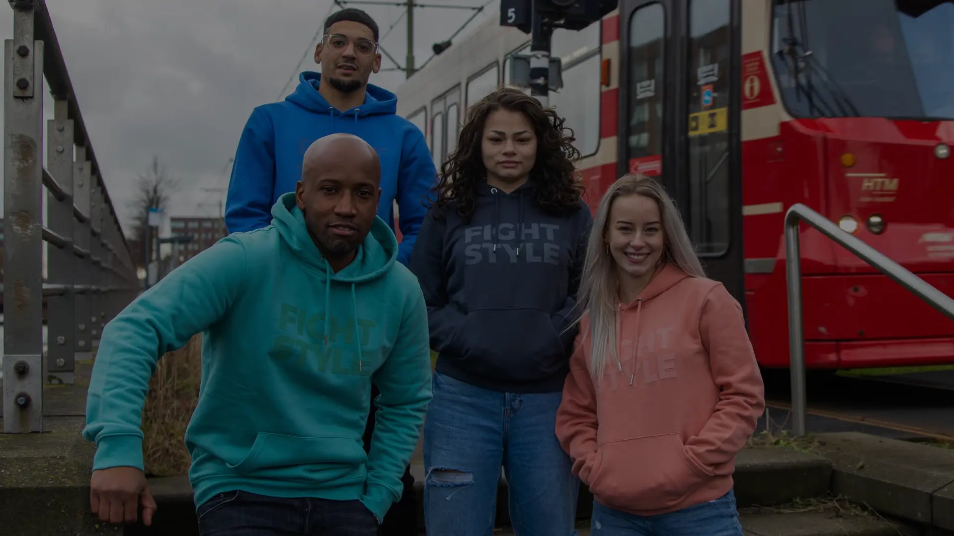 Vier personen, gekleed in 'Fight Style' hoodies in verschillende kleuren, poseren voor een rotsachtige achtergrond.