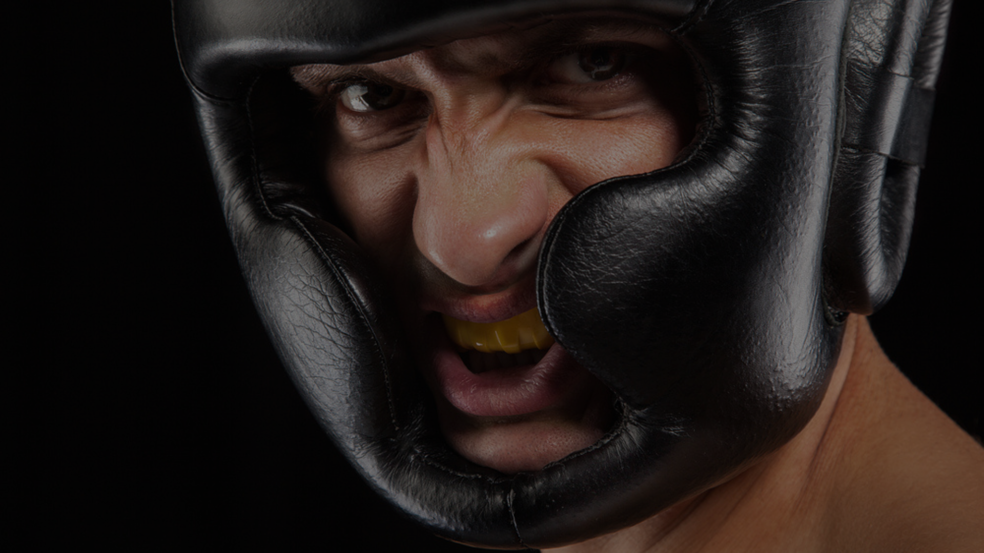 Close-up van een sporter met een zwarte lederen hoofdbeschermer en bitje, klaar voor intensieve boks- of sparringtraining.