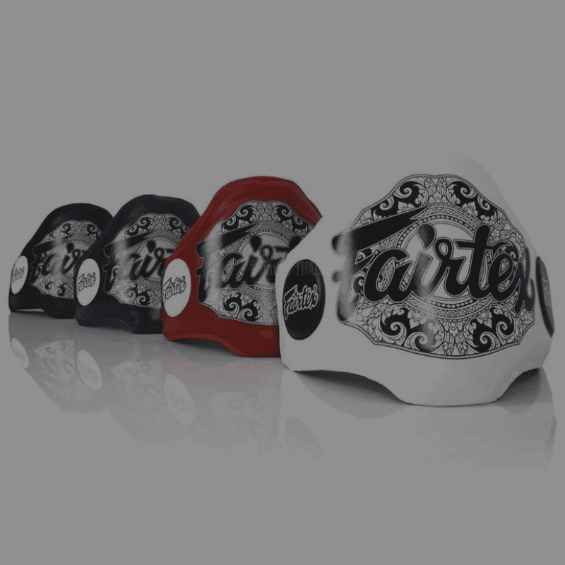 Verschillende gekleurde belly pads met sierlijke witte patronen en het woord "Fairtex" prominent weergegeven, geordend tegen een donkere achtergrond.