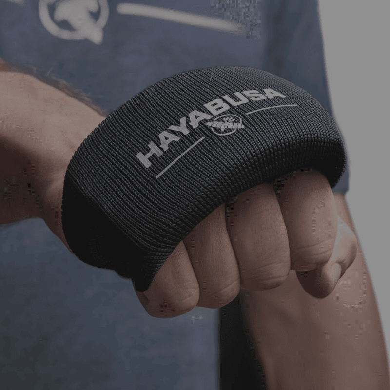 Een close-up van een hand met een zwarte, gewatteerde knokkelbeschermer met een logo.