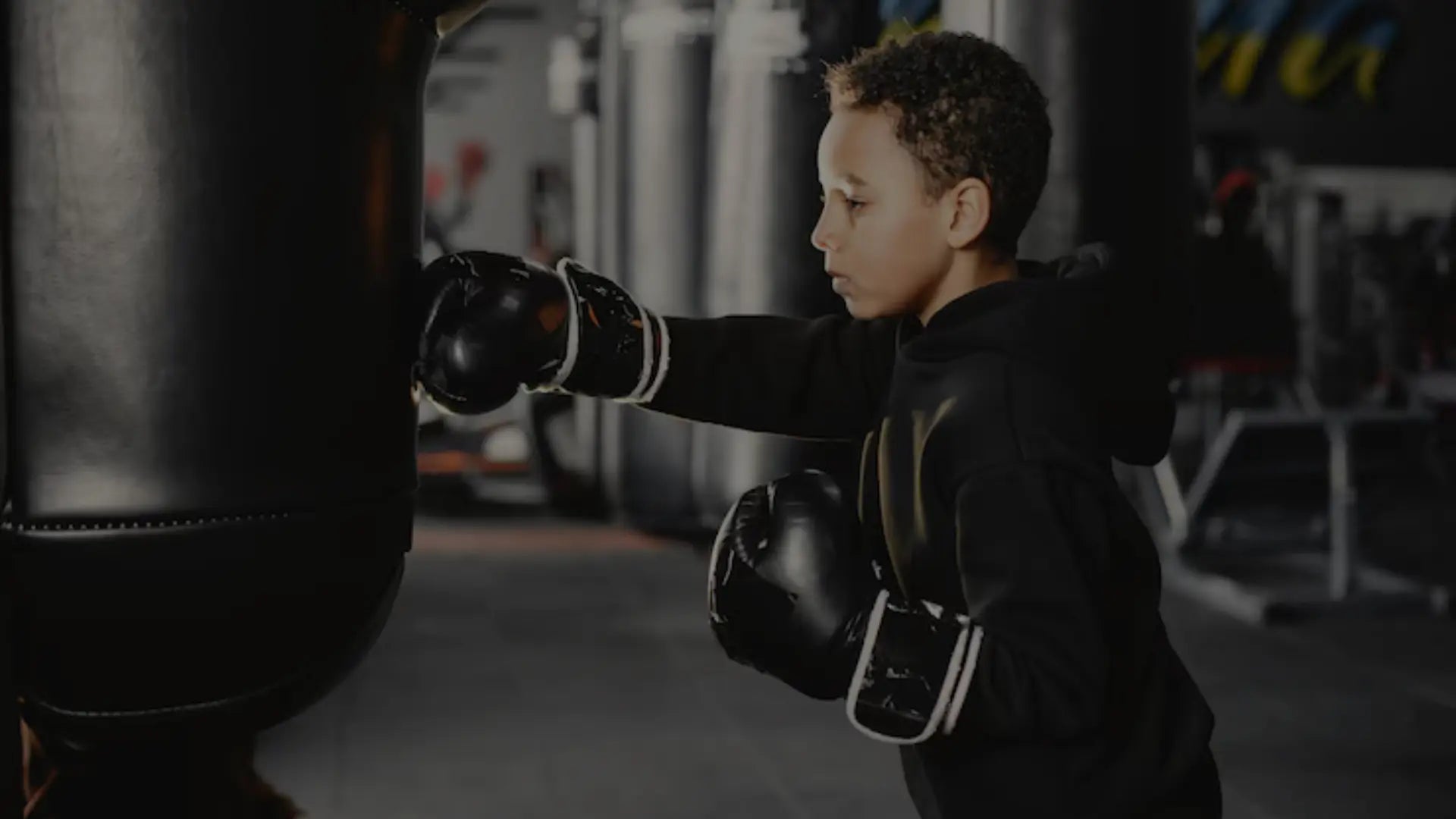 Een jonge jongen met bokshandschoenen staat serieus in een boksring, met posters op de achtergrond.