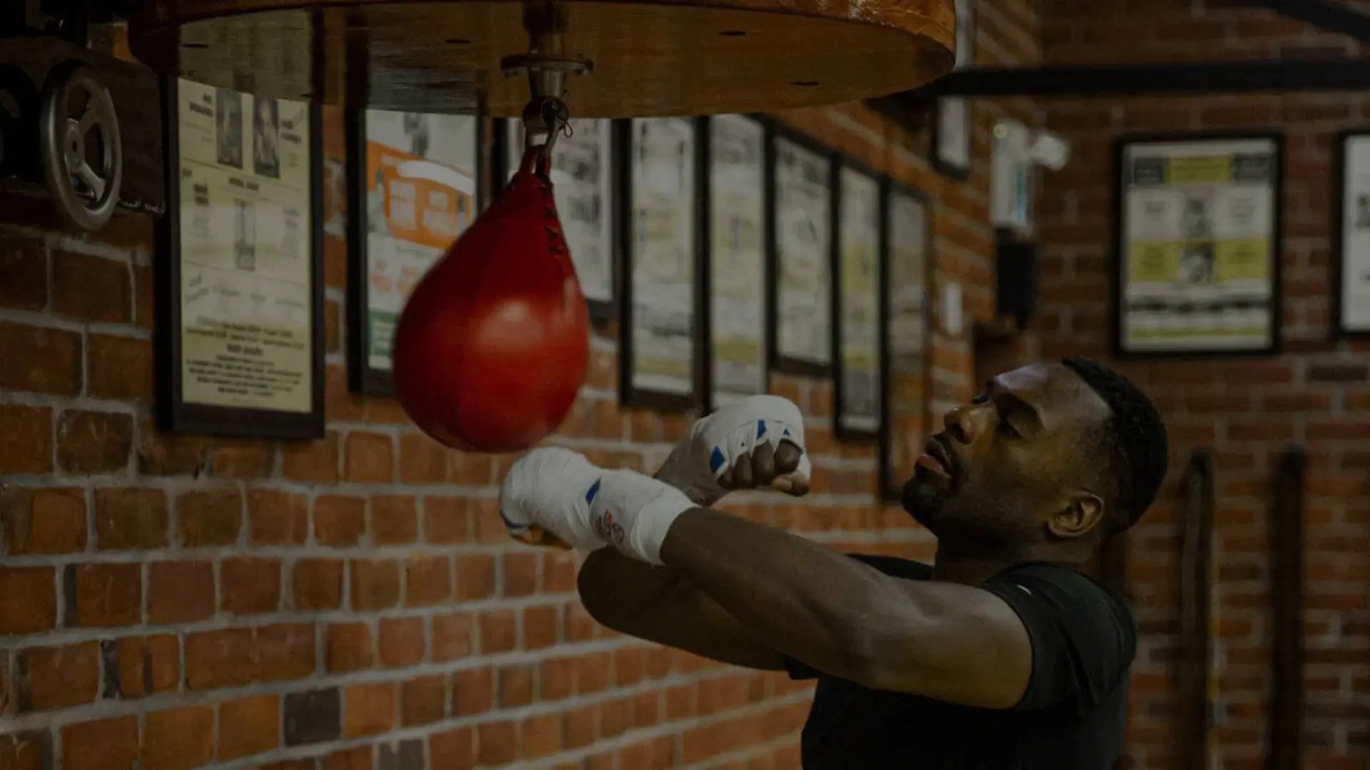 Een persoon in een sportschool doet een kettlebell oefening; we zien de persoon vanuit een laag standpunt, gefocust op de kettlebell en de onderste helft van het lichaam, met sportschoenen aan en een ander persoon op de achtergrond.