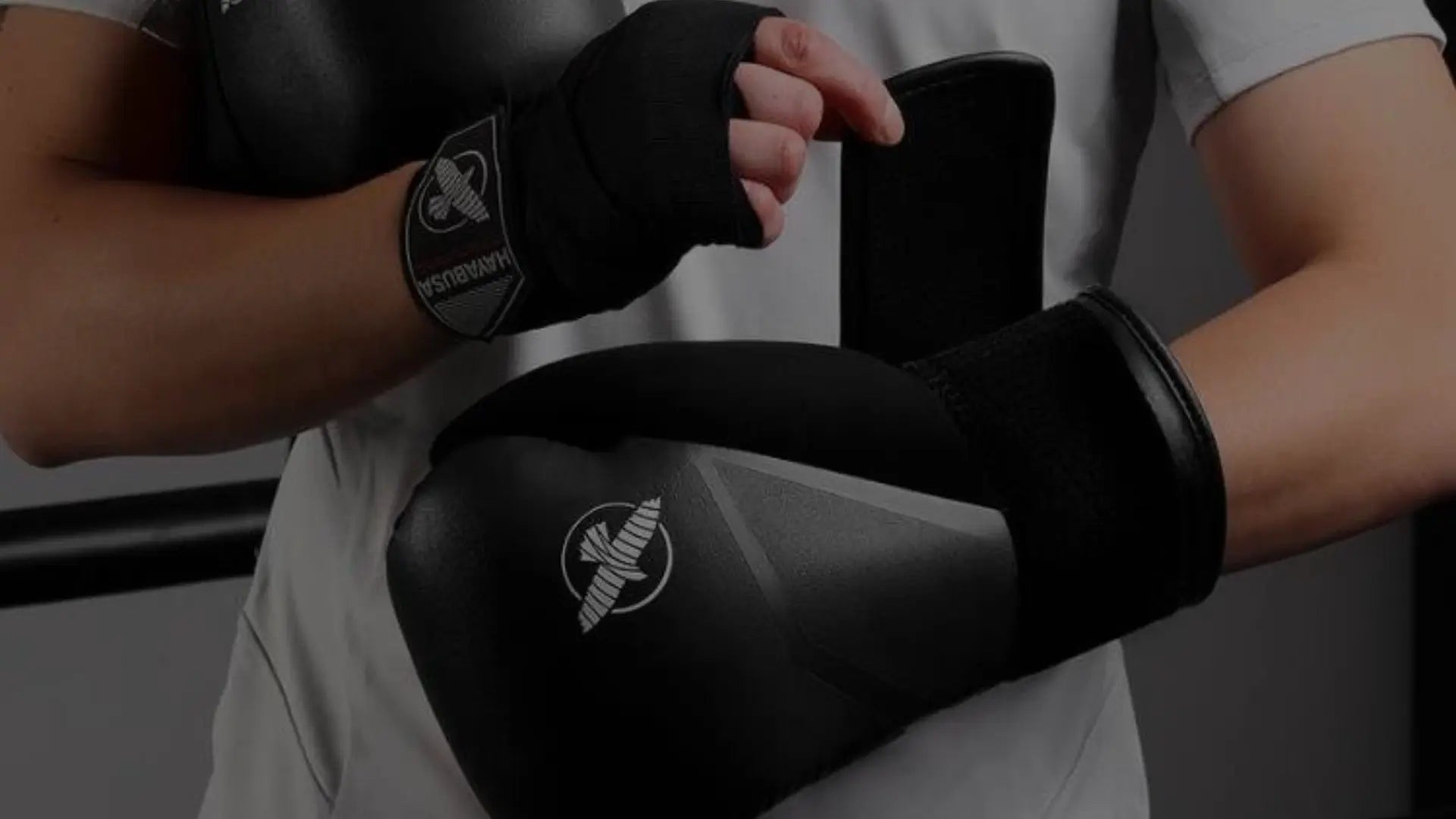 Close-up van een sporter die zwarte bokshandschoenen van Hayabusa sluit, terwijl zwarte handwraps om de polsen extra ondersteuning bieden.