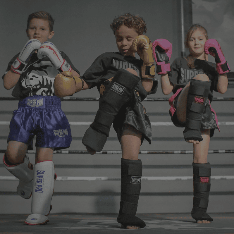 Drie kinderen in vechtsportuitrusting, twee met bokshandschoenen en één met scheenbeschermers.