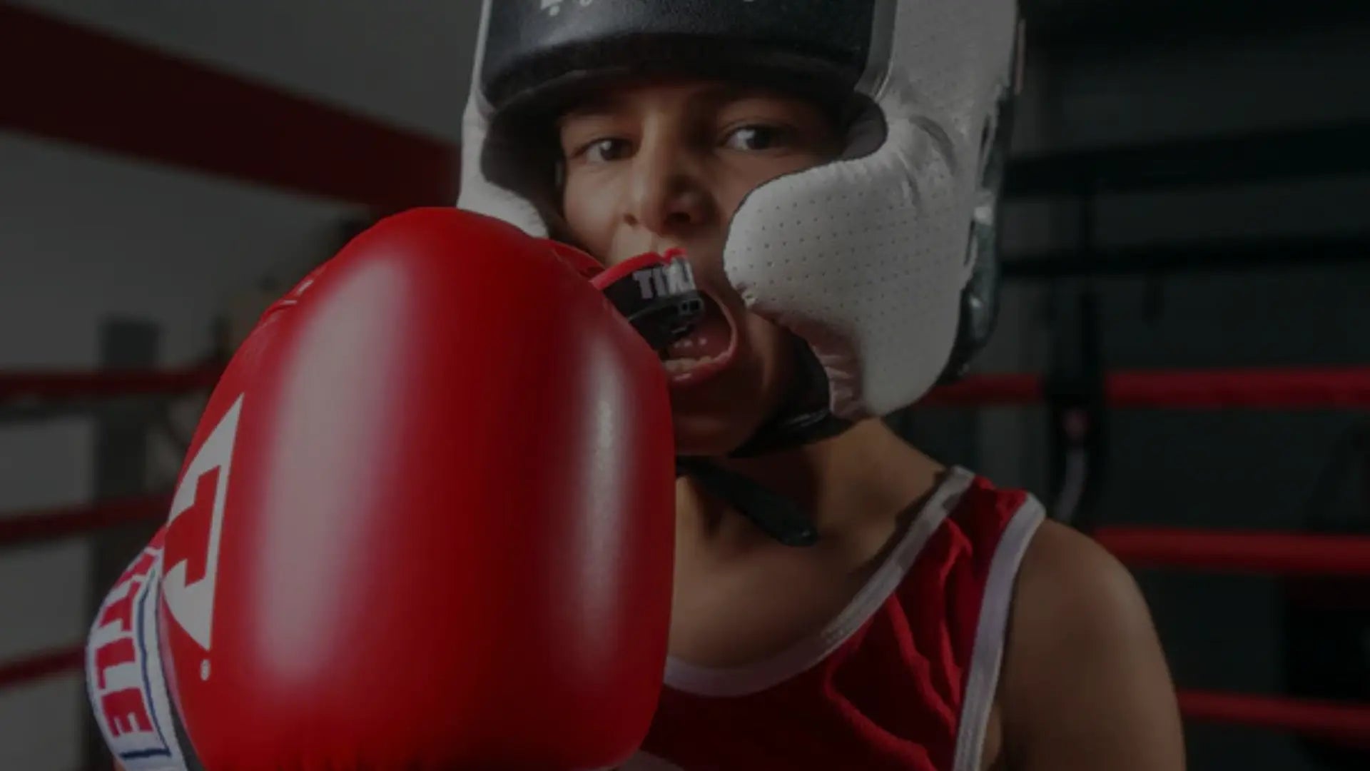 Een jonge jongen met een vochtige huid en een mondbeschermer, kijkt ernstig naar de camera.
