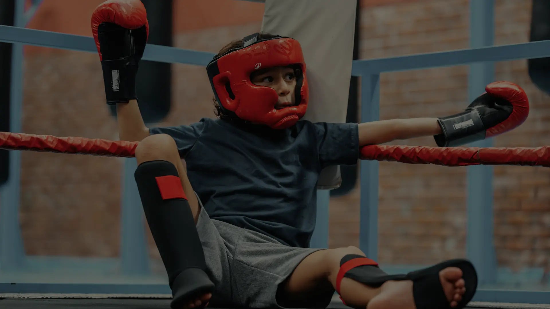 Een tiener met hoofdbescherming en bokshandschoenen kijkt bedachtzaam terzijde.