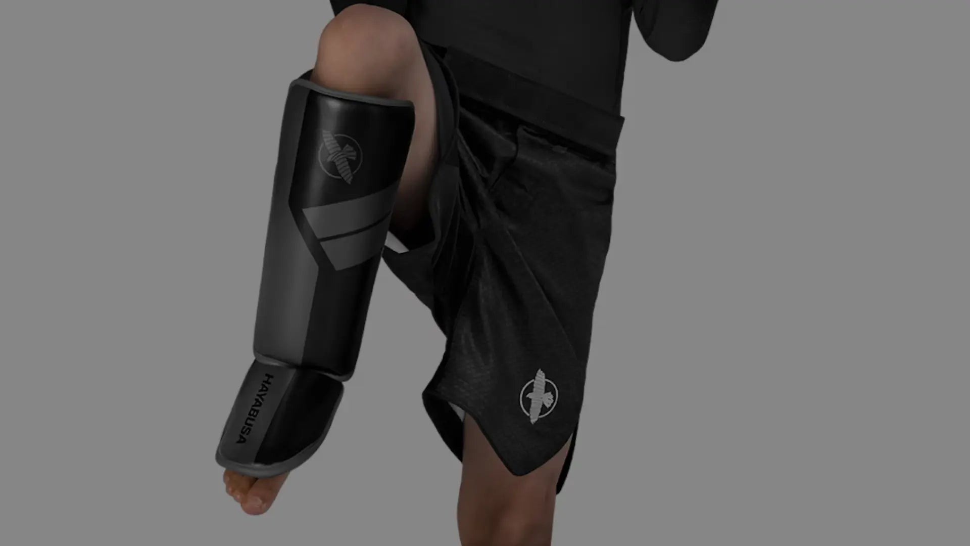 Een jongen in een vechthouding draagt bokshandschoenen en scheenbeschermers, klaar voor training.