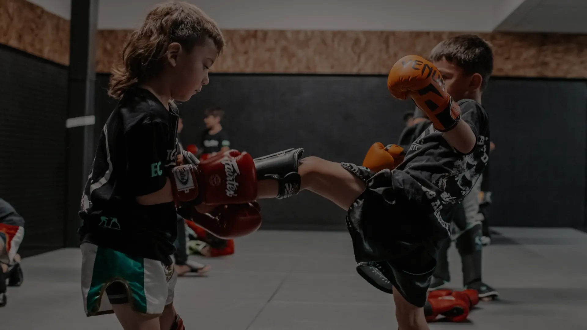 Kinderen trainen kickboksen in de gym, met bokshandschoenen en beschermende gear tijdens een jeugdtraining.