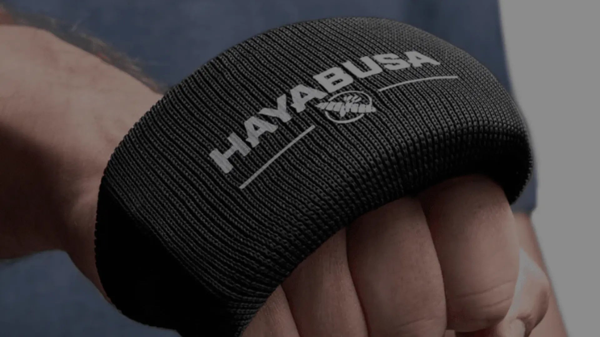 Een close-up van een hand met een zwarte, gewatteerde knokkelbeschermer met een logo.