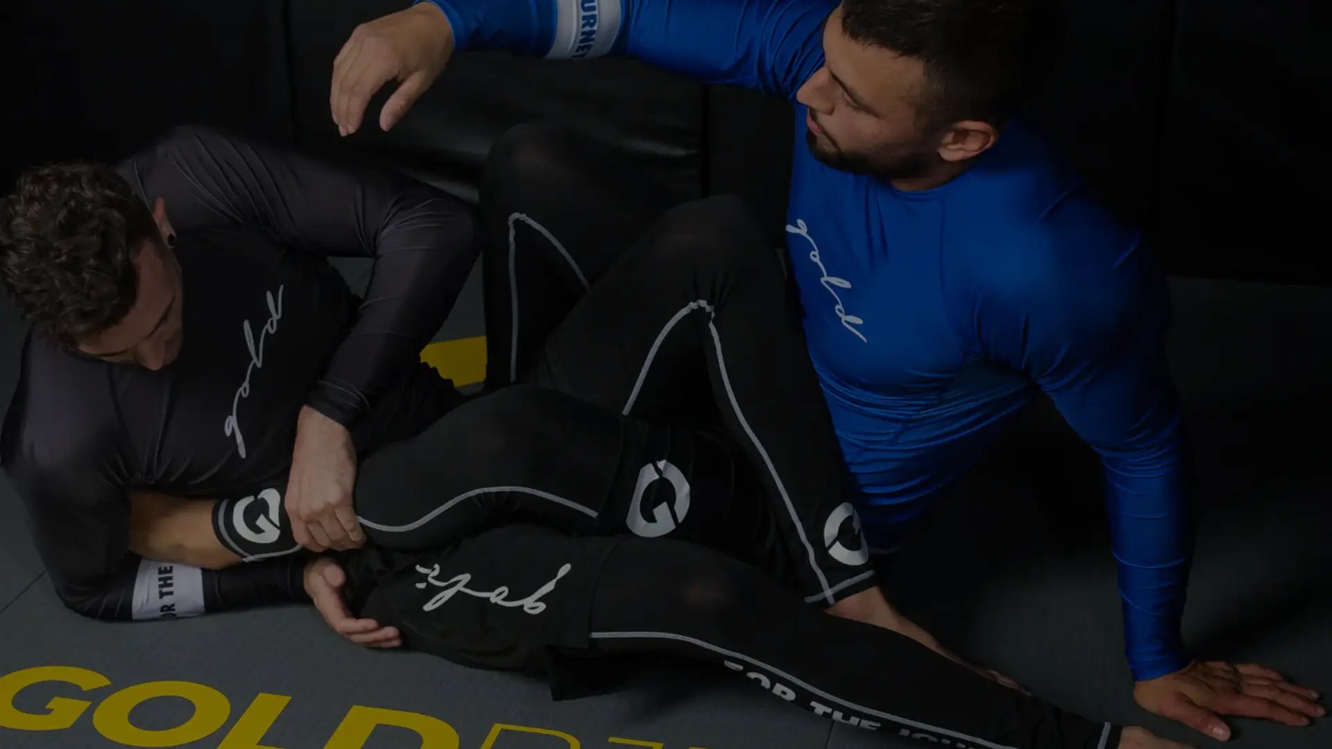 Een man staat zelfverzekerd op een trap voor een tempel, gekleed in een getailleerde legging en een sportshirt met de tekst "KING".