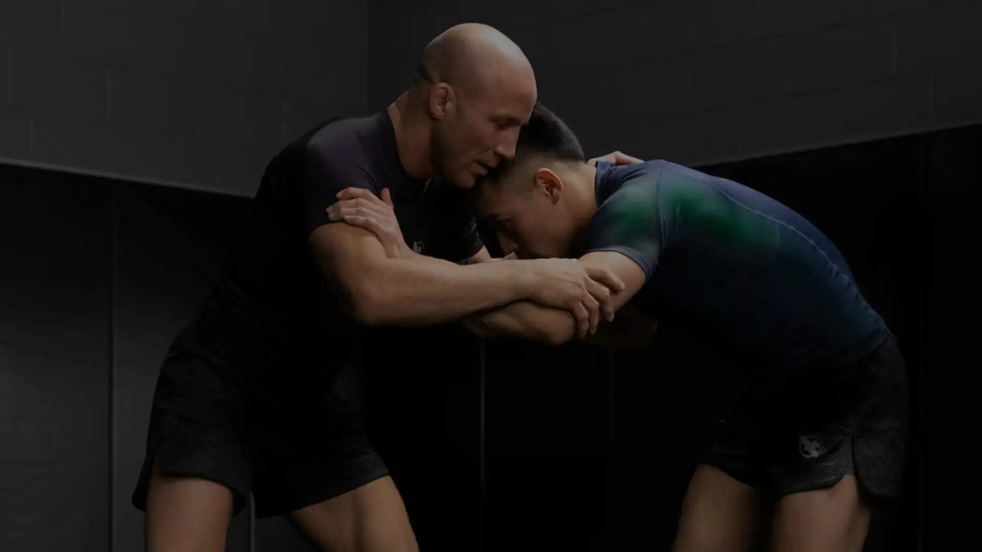 Twee sporters trainen staand grappling in een gym en werken vanuit de clinch aan controle en balans. Beiden dragen aansluitende sportkleding sets die bewegingsvrijheid en comfort bieden tijdens intensieve trainingsvormen zoals worstelen en BJJ.