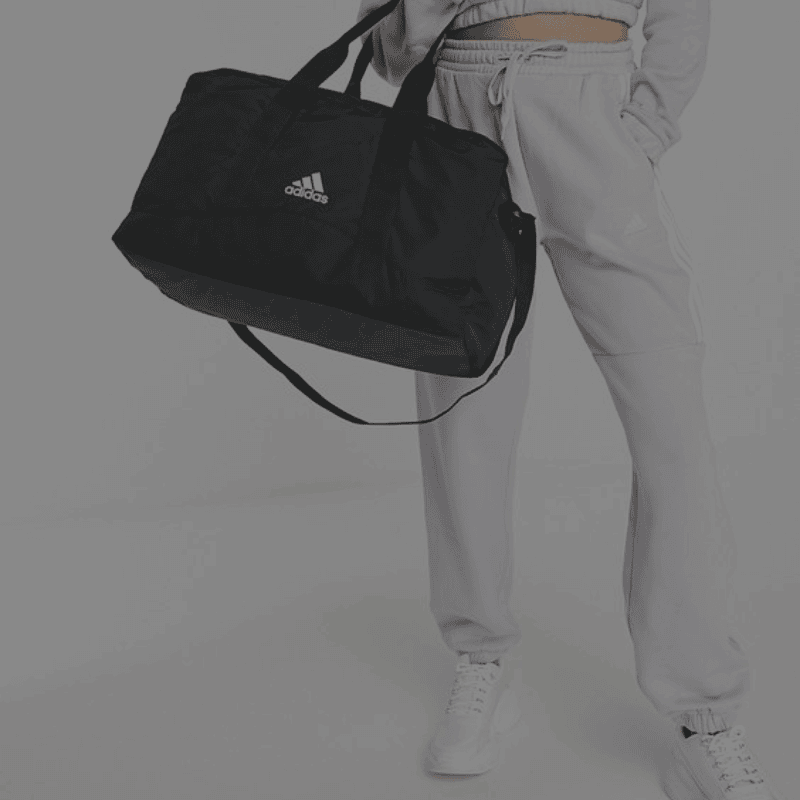 Iemand gekleed in casual sportkleding houdt een zwarte sporttas vast.