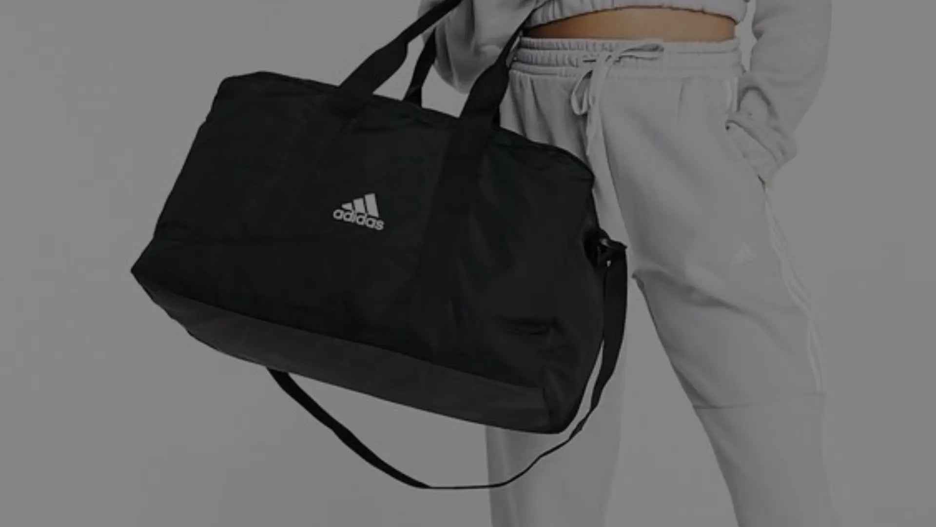 Iemand gekleed in casualsportkleding  houdt een zwarte sporttas vast.