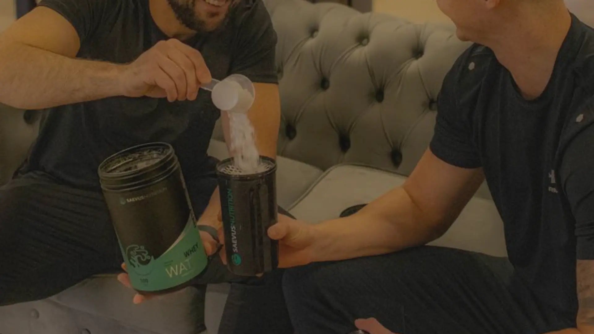 Twee mensen in een sportschool, lachend terwijl ze sportvoedingssupplementen voorbereiden.