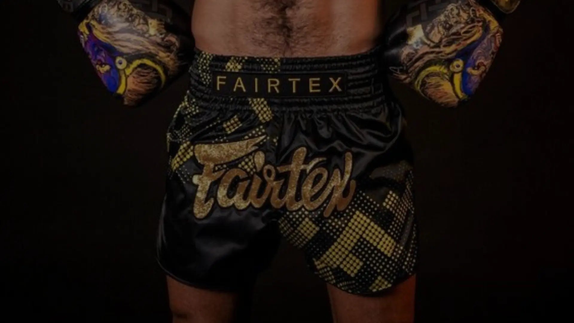 Een getrainde mannelijke vechtsporter van achteren gezien, met Fairtex bokshandschoenen en bijpassende shorts, poseert met gebalde vuisten en opgeheven armen om zijn gespierde rug en schouders te tonen.