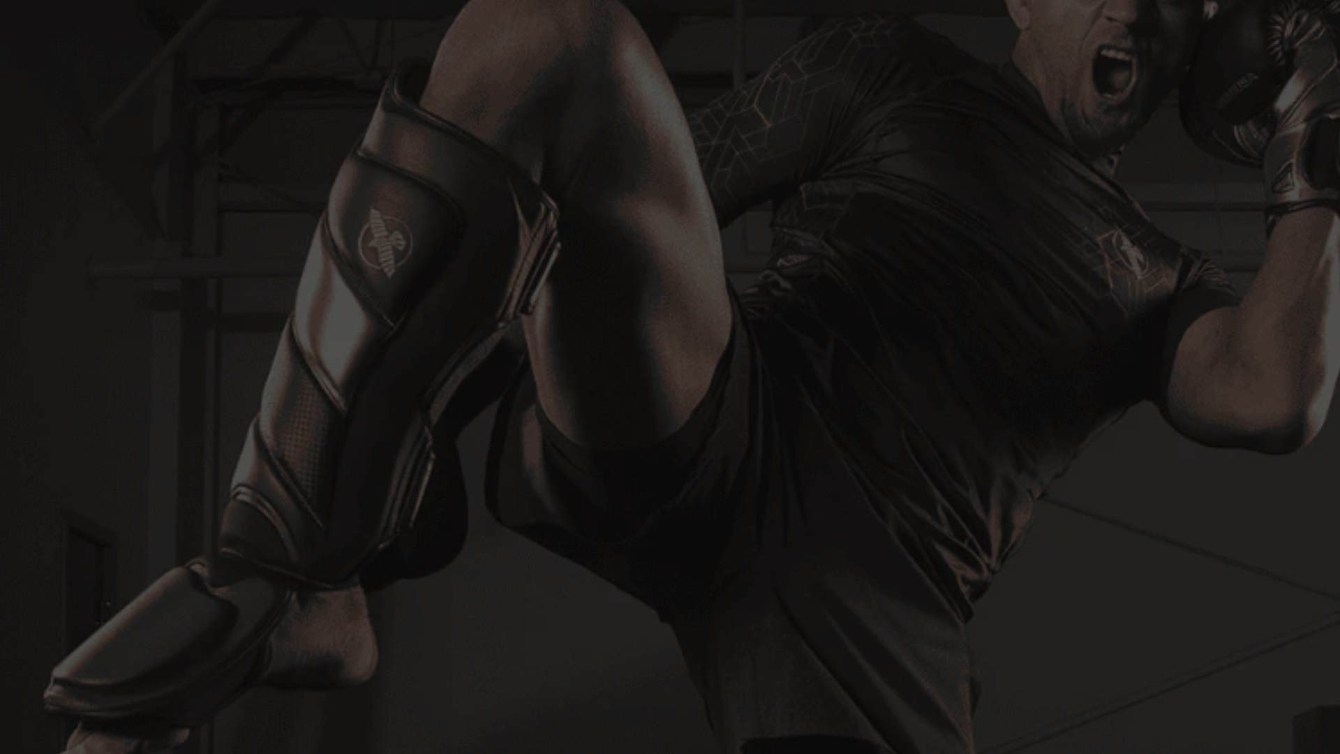 Een atleet in een sportieve outfit voert een hoge trap uit met beschermers om de scheen en knieën en bokshandschoenen aan.