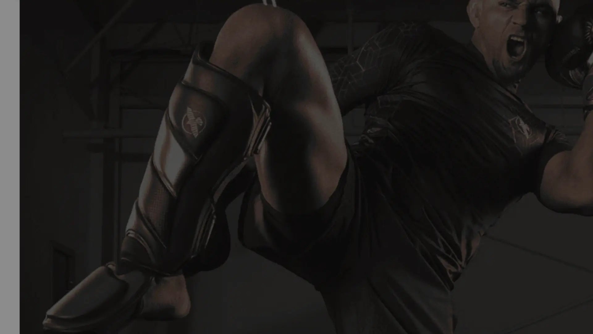 Een atleet in een sportieve outfit voert een hoge trap uit met beschermers om de scheen en knieën en bokshandschoenen aan.