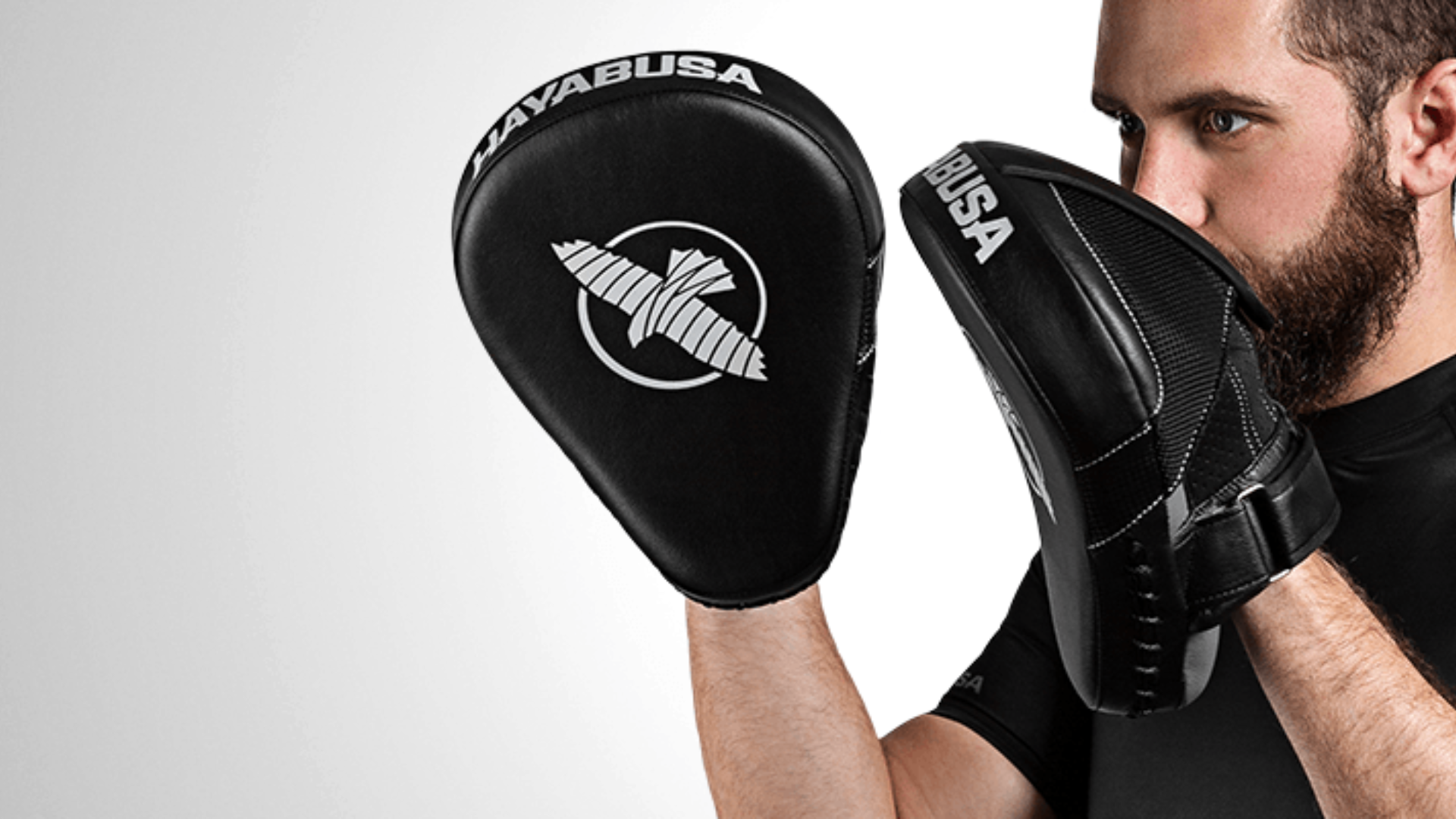 Een sporter traint buiten met zwarte bokshandschoenen en slaat op handpads die worden vastgehouden door een partner in donkere sportkleding.