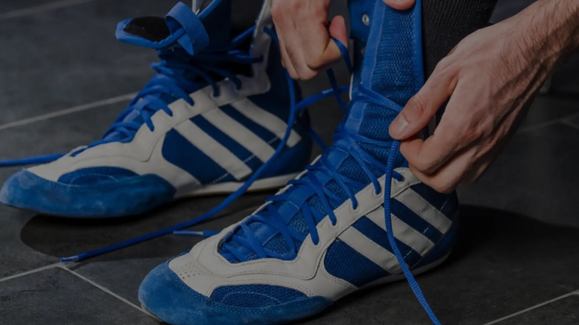 Close-up van een sporter die de veters strikt van blauwe en witte worstelschoenen ter voorbereiding op een training of wedstrijd.