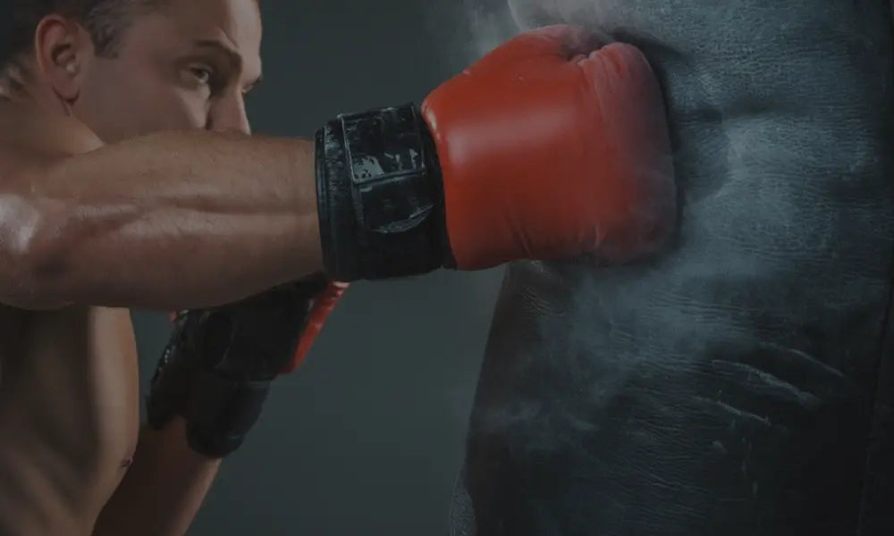 Een rode bokshandschoen raakt een stootkussen met een zichtbare stofwolk, wat duidt op een krachtige impact.