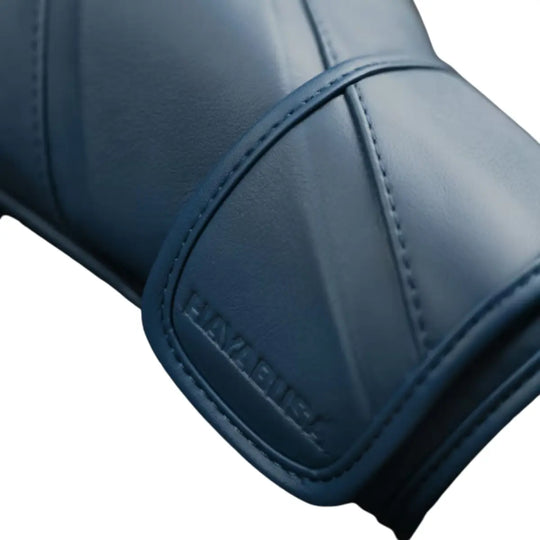 Close-up van de polssluiting van een bokshandschoen in een diepe, matte blauwtint. De subtiele ton-sur-ton branding en strakke stiknaden benadrukken het minimalistische en moderne design. De brede klittenbandsluiting zorgt voor stevige polsondersteuning en een stabiele, comfortabele pasvorm tijdens intensieve trainingen.