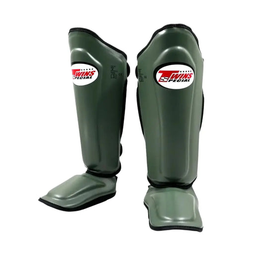 Twins Special SGL7 scheenbeschermers in olijfgroen met zwart afgewerkte randen en wit-rood logo op het scheenbeen. Voorzien van stevige padding en geïntegreerde voetbescherming voor optimale schokabsorptie tijdens kickbokstraining en sparren in de gym.