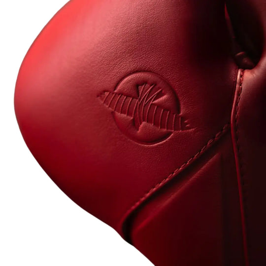 Close-up van de knokkelzijde van een rode bokshandschoen met subtiel reliëflogo in dezelfde kleur. De matte afwerking en fijne materiaalstructuur geven de handschoen een luxe en minimalistische uitstraling. De strakke stiknaden en ergonomische vorm benadrukken de hoogwaardige afwerking en stevige constructie. Een krachtig design dat perfect past bij intensieve bokstrainingen in de gym.
