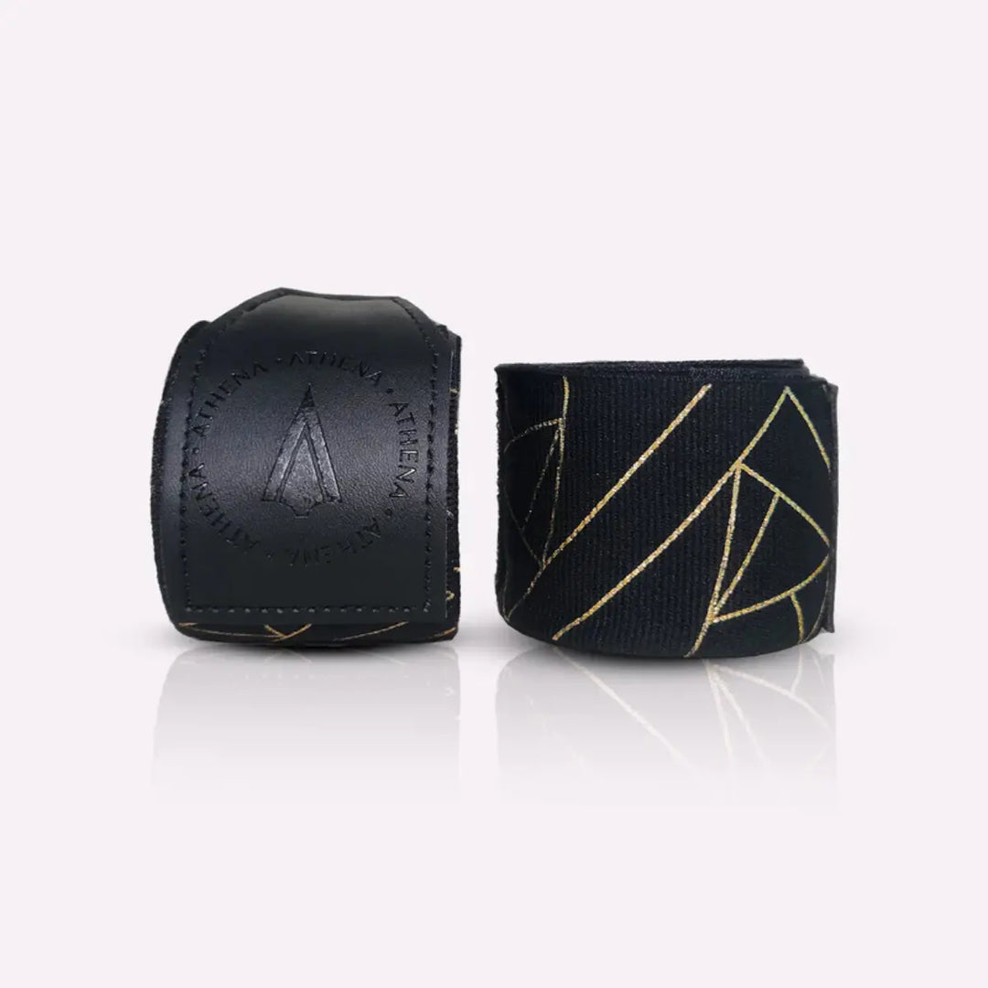 Athena Fightwear handwraps in opgerolde vorm naast de polssluiting van kunstleer met het logo. Het zwart-met-goud patroon geeft een luxe en moderne uitstraling. De stevige sluiting zorgt voor een veilige fixatie tijdens bokstraining. Ideaal voor ondersteuning van handen en polsen.
