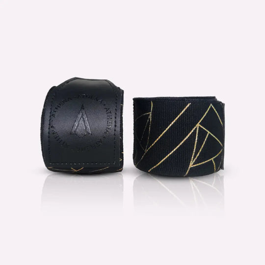 Athena Fightwear handwraps in opgerolde vorm naast de polssluiting van kunstleer met het logo. Het zwart-met-goud patroon geeft een luxe en moderne uitstraling. De stevige sluiting zorgt voor een veilige fixatie tijdens bokstraining. Ideaal voor ondersteuning van handen en polsen.