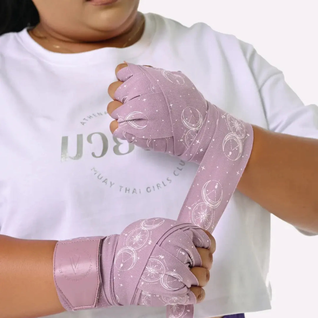 Vrouw wikkelt Athena Fightwear Serena Mauve bandages om haar handen, lavendelkleurig met maan- en sterrenprint.