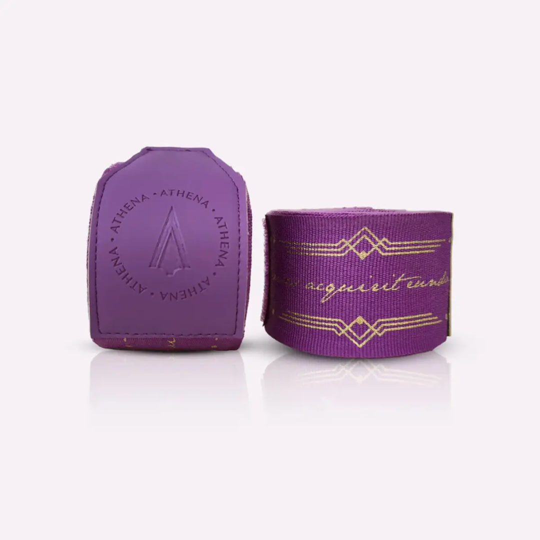 Athena Fightwear Diana Violet handwraps in opgerolde vorm naast de paarse polssluiting. De gouden patronen lopen stijlvol over de bandage heen. De stevige sluiting zorgt voor een veilige en comfortabele pasvorm tijdens training.