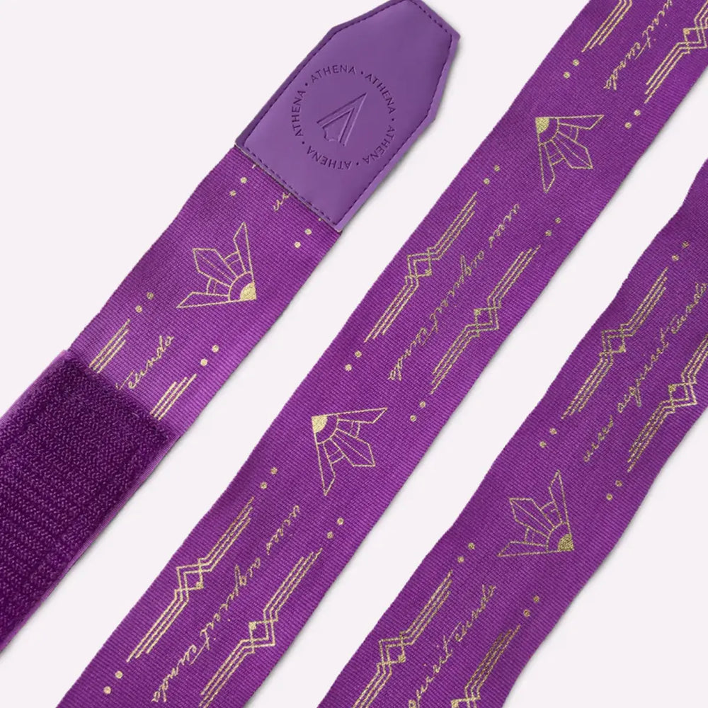 Detailfoto van de Athena Fightwear Diana Violet handwraps plat neergelegd. De gouden lijnen en decoratieve symbolen zijn duidelijk zichtbaar over de gehele bandage. Het leren uiteinde met het Athena-logo geeft een luxe uitstraling.
